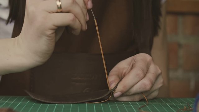 Leather master sewing with needle and strings. Professional female skinner working with genuine leather at workshop. Handmade and leatherwork concept.