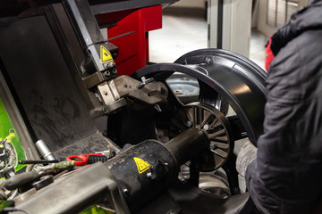 The process of repairing an automobile wheel using a special press on a machine for straightening disks for vehicles after damage in a pit on the road in the workshop by worker hands in gloves.