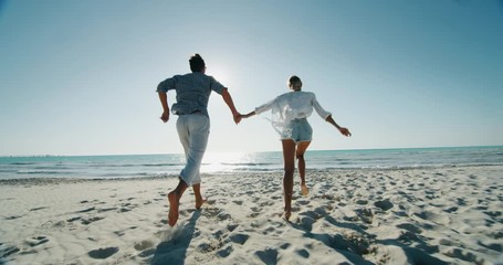 Slow motion of young carefree couple is having fun and enjoying their summer vacation together on a beach with a sea in a sunny day. - Powered by Adobe