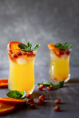 Orange drink with ice, mint and pomegranate on grey wooden background