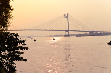 Sunset over Vidyasagar Setu (a modern Cantilever Spar Cable-Stayed Bridge) in a summer evening on the river Hooghly. Silhouette view from distant. Howrah city, Kolkata, West Bengal, India, South Asia.