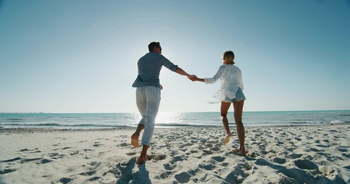 Slow motion of young carefree couple is having fun and enjoying their summer vacation together on a beach with a sea in a sunny day.