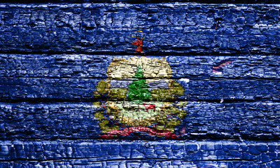 The national flag of the US state Vermont in against a black charred wooden wall on the day of...