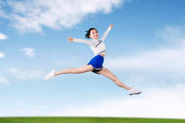 Fototapeta na wymiar Cheerleader girl jumps and doing splits in the field