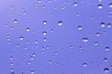 Rain drops with selective focus on transparent glass. Glass surface with water drops, violet toned. Window with raindrops. water drops on glass