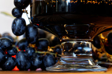 Homemade wine, juice or tincture in a transparent glass on a background of black grapes. Farm harvest on the counter of the fair