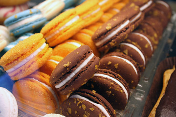 Colorful cakes macaron aka French macarons lie on the counter. Orange and brown macarons lie in rows.