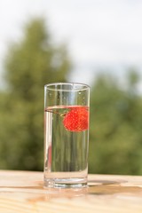 A transparent glass with water and ripe strawberries in it.