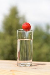 Ripe strawberry berry drops in a transparent glass with water on a wooden board