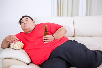 Overweight man eats popcorn and drinks beer