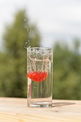 A transparent glass with water and ripe strawberries in it.