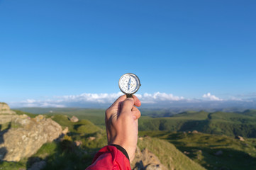 Man searching direction with a compass in his hand in the summer mountains point of view. Direction...