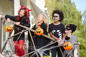 Fototapeta premium Multi-ethnic group of happy children posing on decorated porch while trick or treating together in Halloween season