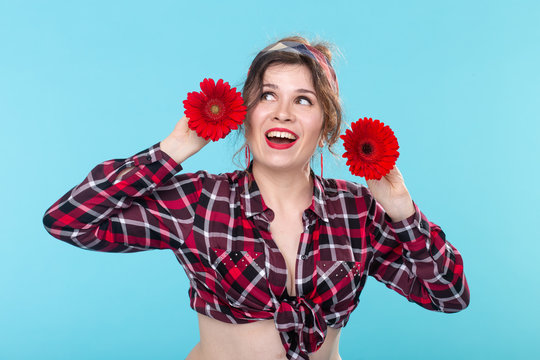 Close-up portrait of a beautiful young woman holding red flowers with different hearts in the hands posing on a blue background. Concept of differences and delicate nuances.
