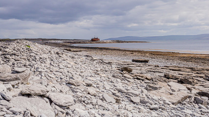 View of the empty limestone rocky beach of Inis Oirr Island with the sea and the Plassey shipwreck in the background on a cloudy day, Inisheer is a small island in the west of the coast of Ireland