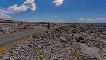 Female cyclist on a rural road between limestone rocks on the coast of Inis Oirr Island, wonderful...