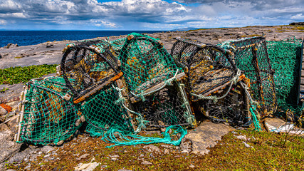 Accumulation of old and broken lobster / crab cages or fishing traps found on the coast in Inis Oirr island, the ocean in the background at Inisheer, an island in the west of the coast of Ireland