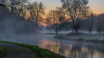sunrise in winter at a lake with haze and a path in Elsloo South Limburg in the Netherlands Holland