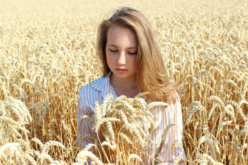 Portrait of a pretty woman sitting in a summer wheat field and looking down. People, nature, freedom and travel concept.