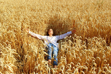 Full length shot of a pretty teenage girl enjoying the outdoors. Caucasian girl wearing a blue jeans and white shirt lying in wheat field. People, travel, freedom concept.