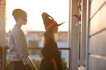 Side view portrait of two children waiting by door while trick or treating on Halloween, copy space