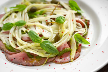 Fennel salad with beef carpaccio, Basil and pesto on a white plate. Italian gourmet snack