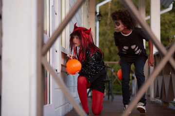 Portrait of two sneaky kids hiding outside house while playing games on Halloween, copy space