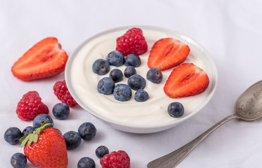 White yogurt in bowl with oatmeal and strawberries, blueberries and raspberries on the top.
