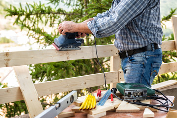 Adult carpenter craftsman with electric sander smoothes the boards of a wooden fence. Housework do it yourself. Stock photography.