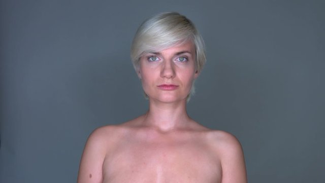 Naked blonde girl is looking straight into the camera. Model shoot. Face potrait with gray background.