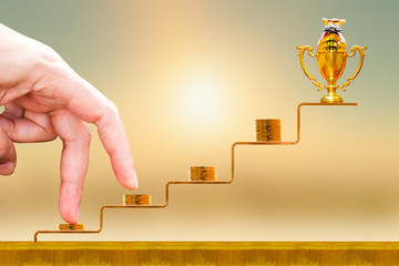 Close up of hand with climb up on a stacking five gold coin with growing on golden steps and trophy...