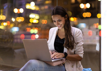 Young woman working on her laptop in the city at night