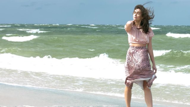 Slow motion shot of a trendy young woman walking by the ocean on a windy day