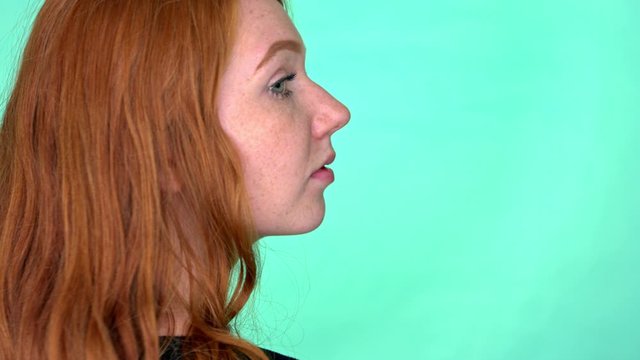 Slow motion portrait red haired young woman turns head and looks over her should direct to camera in studio