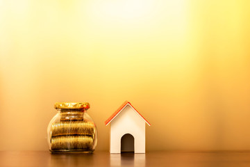 Wooden house model and gold coin in the bottle bank with growing interest on brown background, Business investment or saving money to buy real estate for family concept.