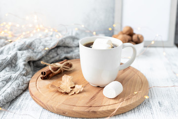 Obraz na płótnie Canvas Mug with coffee and marshmallow, sweater, cinnamon, decorated with led lights. Autumn mood. Cozy autumn composition