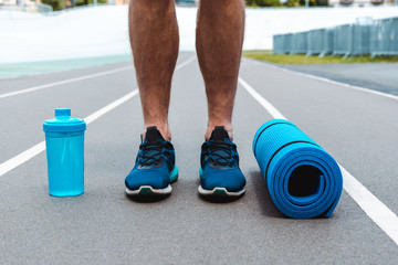 cropped view of young sportsman on running track with sports bottle and blue fitness mat