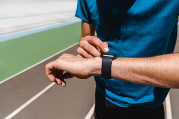 cropped view of young sportsman using smartwatch on running track at sunny day