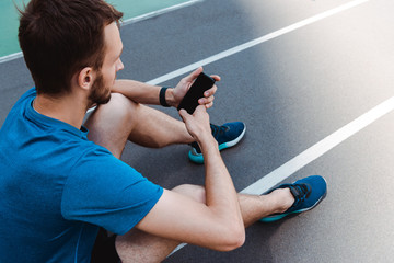 young sportsman sitting on running track and using smartphone