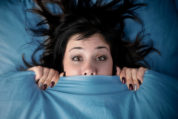 girl hides her face under the covers in bed. a nightmare after watching a horror movie. fear of...
