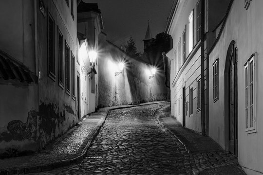 Fototapeta Hidden fairytale street in Prague Czech Republic Novy Svet quarter enlightened by street lamps during night black and white