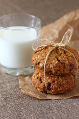 Oatmeal cookies two pieces tied with a rope and a glass of milk on burlap tablecloth.