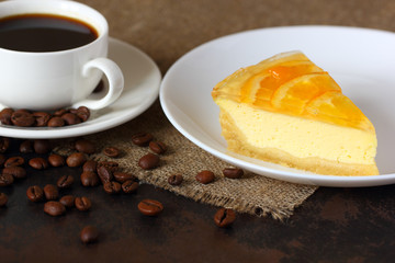 Cheesecake with oranges on a white plate, coffee mug and coffee beans scattered on burlap tablecloth.
