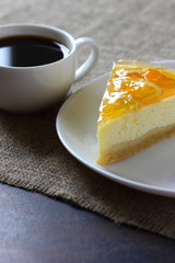 Cheesecake with oranges on a white plate, coffee mug on burlap tablecloth. Vertical frame.