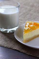 Cheesecake with oranges on a white plate, glass with milk on burlap tablecloth.