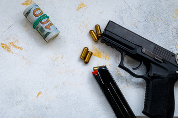 9 mm pistol gun bullets strewn and roll american dollar banknotes on rustic oak table.