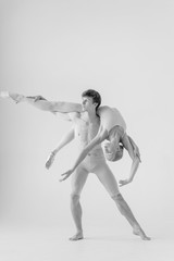 Young couple of modern ballet dancers posing over white studio background
