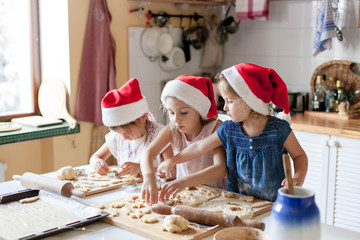 Kids are cooking Christmas cookies in cozy kitchen. Sisters prepare holiday food for family...