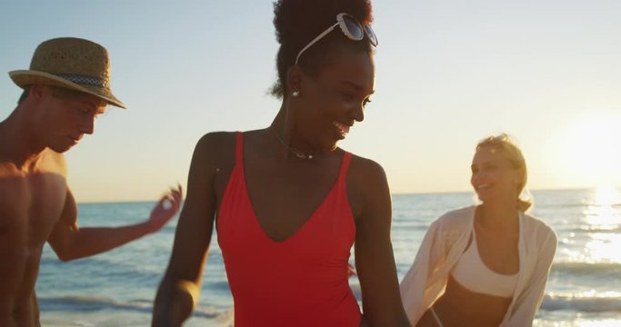 Slow motion close up of young multi-ethnic carefree  friends in swimsuits are having fun and enjoying their summer vacation together on a beach with a sea on a sunset.