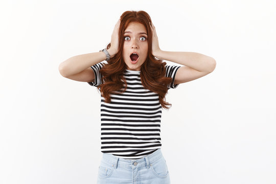 Shocked speechless nervous young cute redhead woman in striped t-shirt grab head in hands, open mouth gasping ambushed and excited, looking embarrassed, remember improtant task, stare camera hopeless
